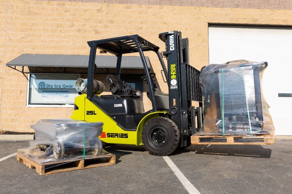 A forklift outside Dry Ice Gear with two pallets of plastic-wrapped rental equipment.